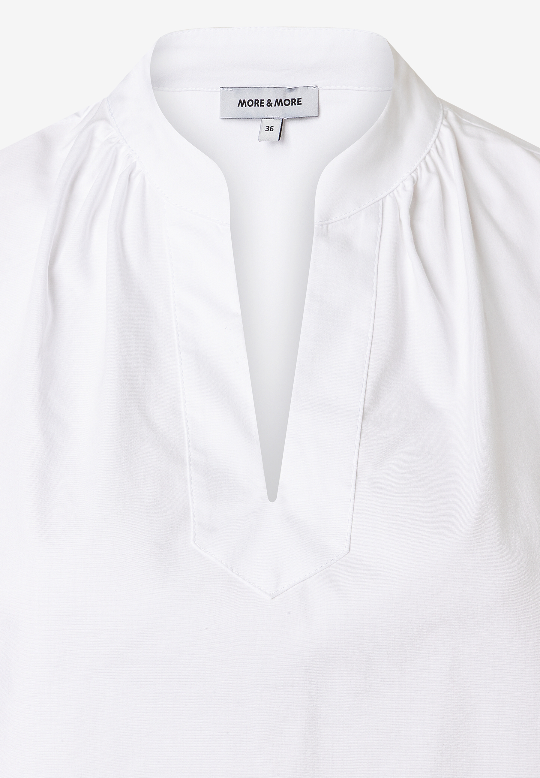 Nahaufnahme einer weißen Bluse von MORE & MORE aus Baumwollmischung mit V-Ausschnitt. Nahaufnahme einer weißen Bluse von MORE & MORE aus Baumwollmischung mit V-Ausschnitt.