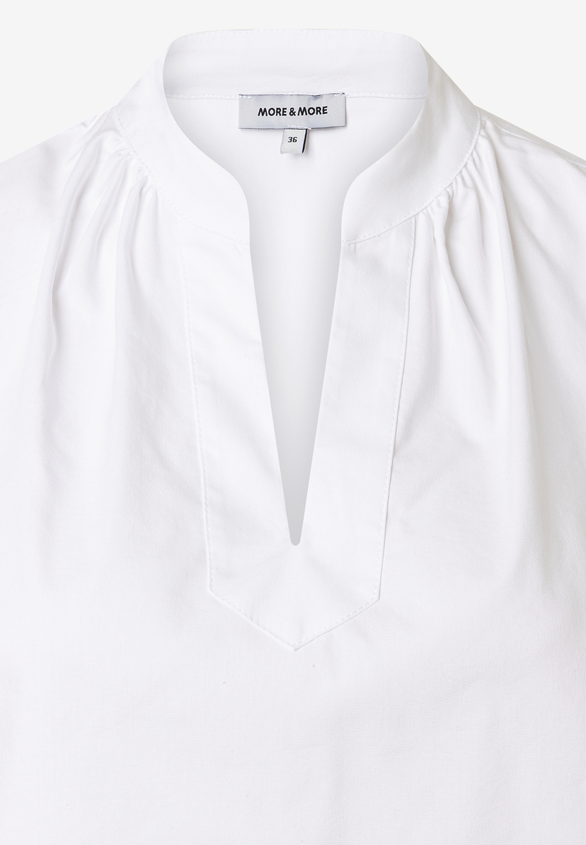 Nahaufnahme einer weißen Bluse von MORE & MORE aus Baumwollmischung mit V-Ausschnitt. Nahaufnahme einer weißen Bluse von MORE & MORE aus Baumwollmischung mit V-Ausschnitt.