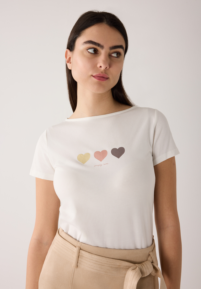 Ein weißes MORE & MORE T-Shirt mit drei Herzen und der Aufschrift "simply love" wird von einer Frau getragen. Ein weißes MORE & MORE T-Shirt mit drei Herzen und der Aufschrift "simply love" wird von einer Frau getragen.