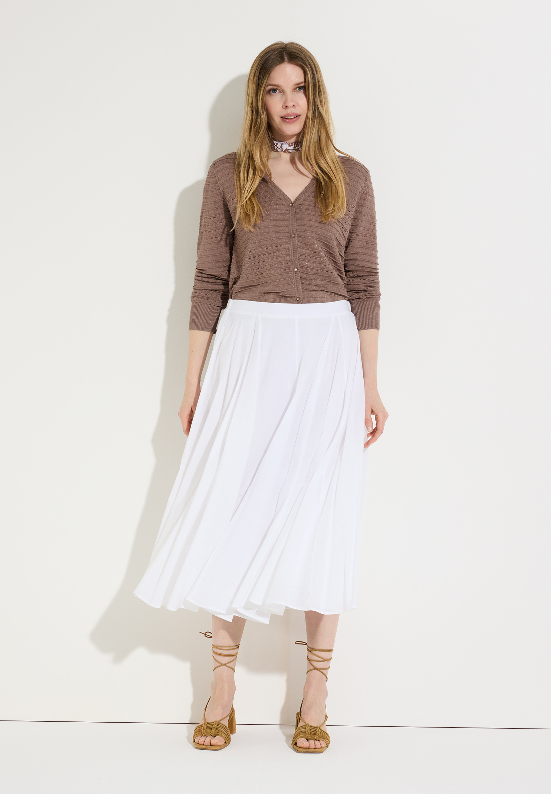 Eine Frau, die einen MORE & MORE Strick-Cardigan und einen weißen Rock vor einem neutralen Hintergrund trägt.