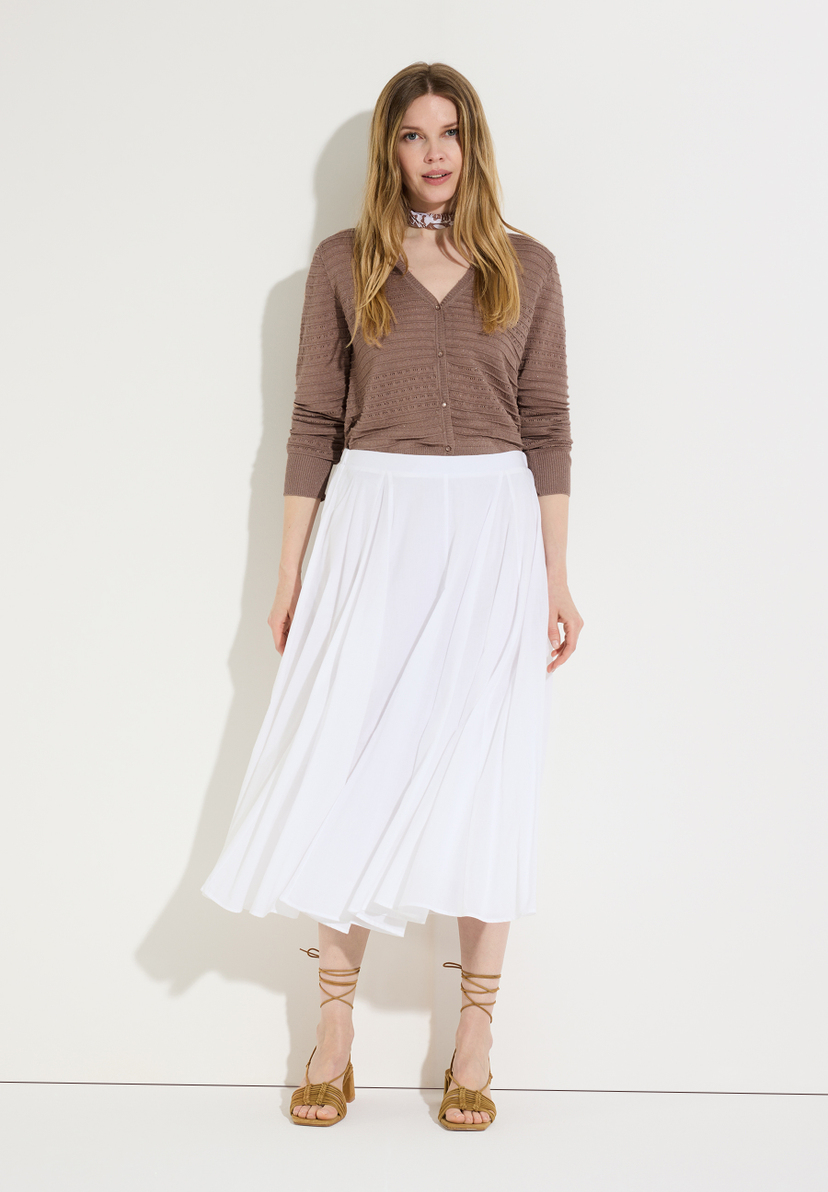Eine Frau, die einen MORE & MORE Strick-Cardigan und einen weißen Rock vor einem neutralen Hintergrund trägt.