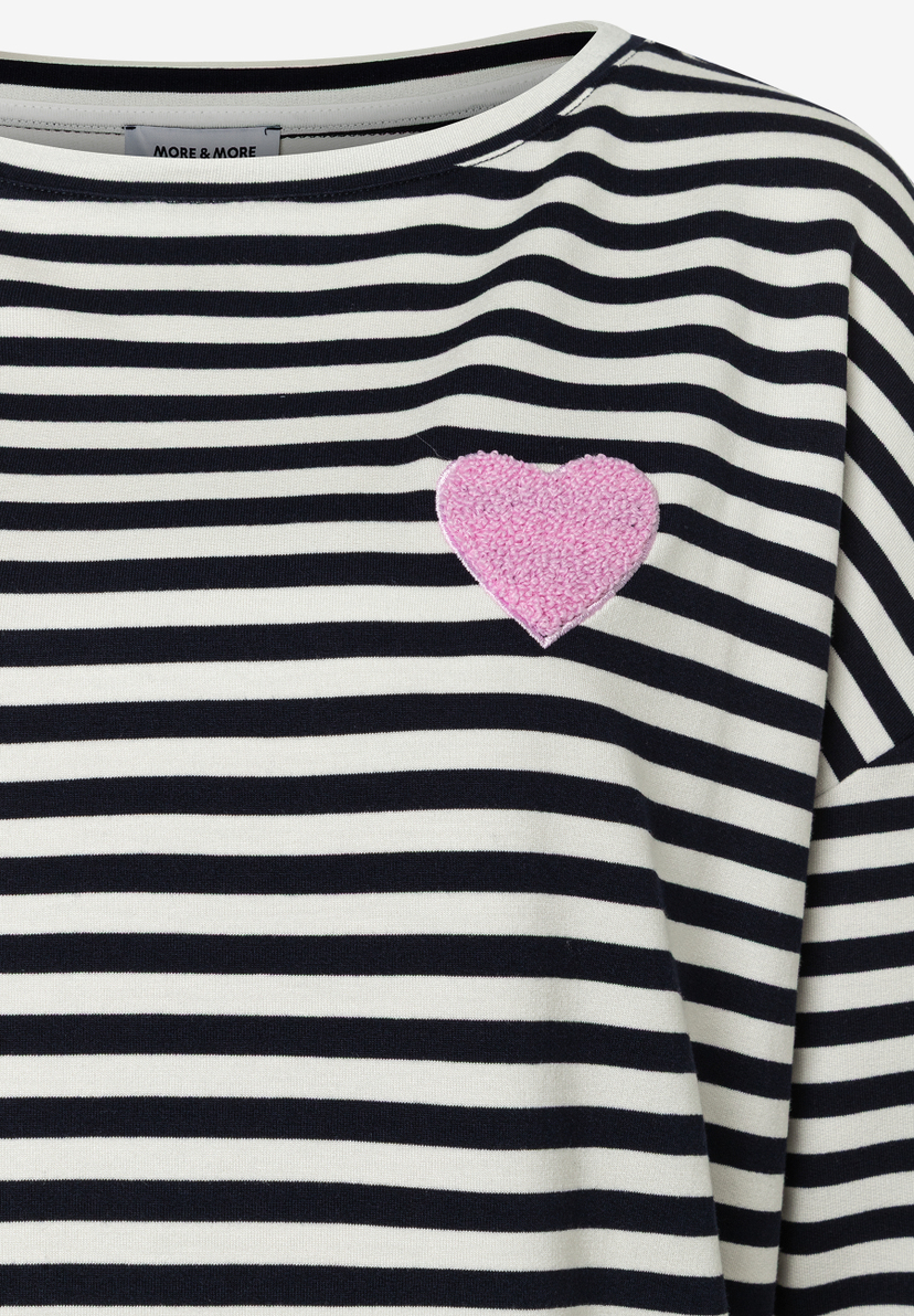 Nahaufnahme eines MORE & MORE T-Shirts mit blauen Streifen und rosafarbenem Herz auf der Brust. Nahaufnahme eines MORE & MORE T-Shirts mit blauen Streifen und rosafarbenem Herz auf der Brust.