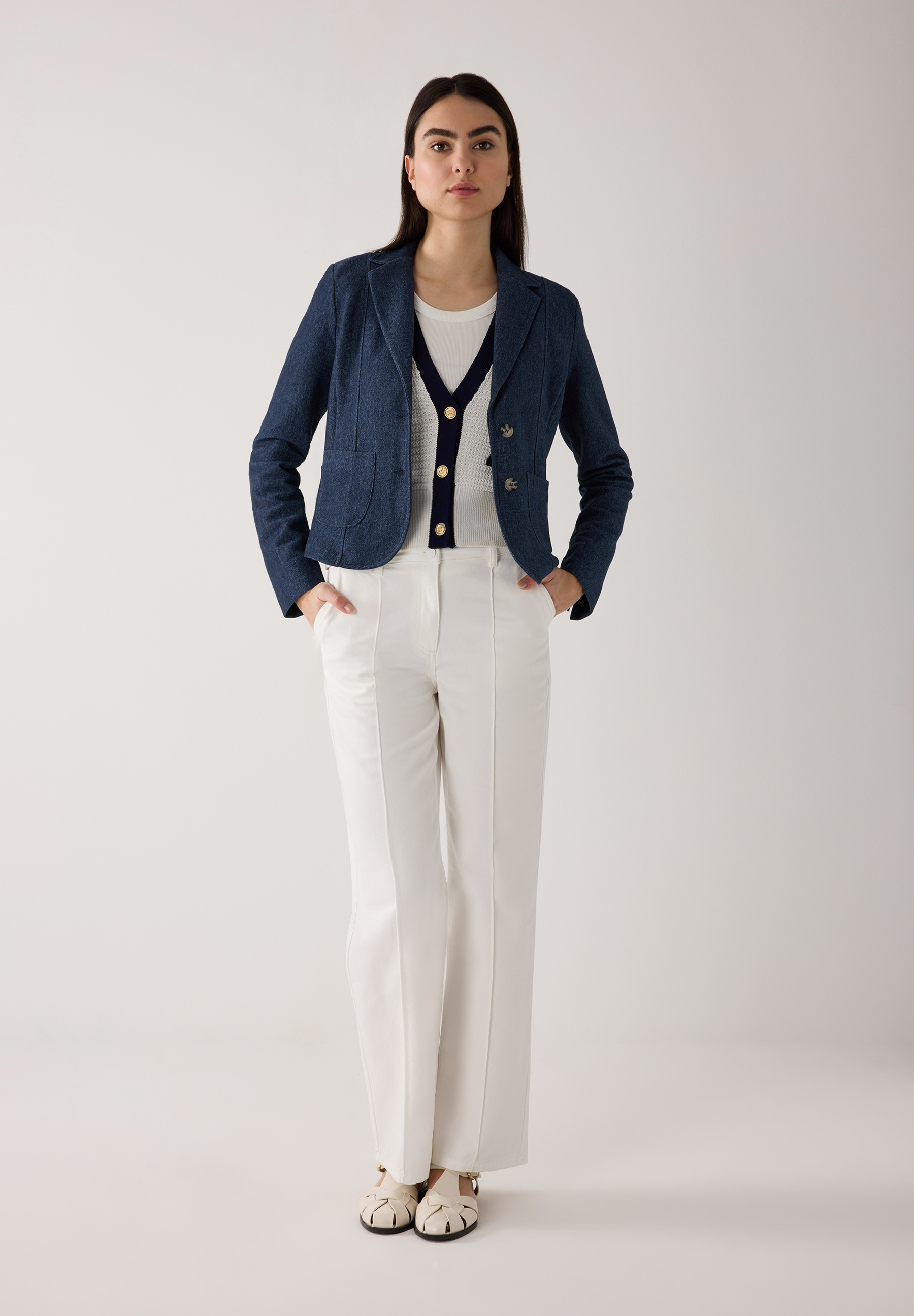 Eine Frau in einem MORE & MORE Blazer, weißem Top und weißen Hosen vor einem hellen Hintergrund. Eine Frau in einem MORE & MORE Blazer, weißem Top und weißen Hosen vor einem hellen Hintergrund.