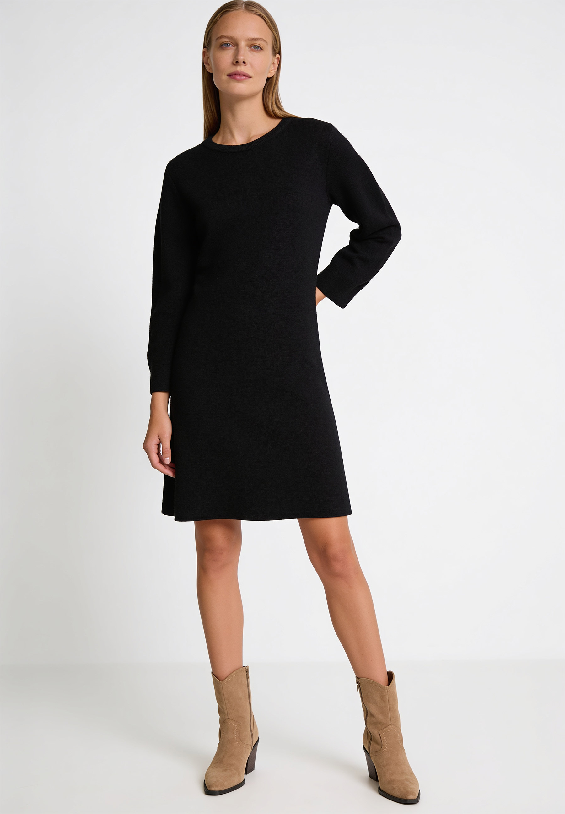 AI generated - MORE & MORE Strickkleid: Eine junge Frau posiert in einem schwarzen, knielangen Strickkleid. Sie trägt dazu Stiefel in Wildlederoptik.