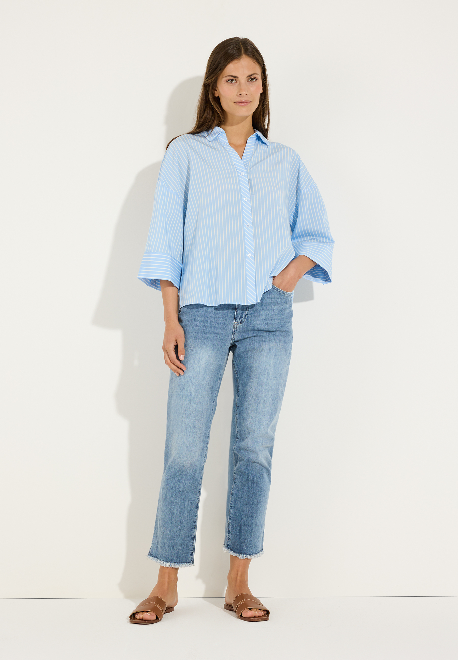 MORE & MORE Popeline-Bluse: Eine junge Frau trägt eine hellblaue Popeline-Bluse mit Nadelstreifen zu Jeans und Ledersandalen. MORE & MORE Popeline-Bluse: Eine junge Frau trägt eine hellblaue Popeline-Bluse mit Nadelstreifen zu Jeans und Ledersandalen.