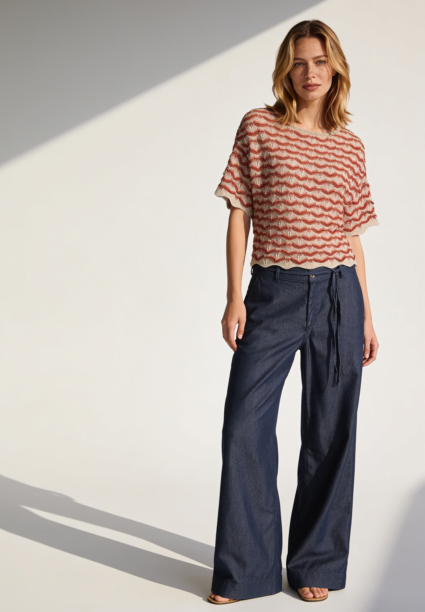 AI generated - MORE & MORE Strukturstrick-Pullover mit rot-weißem Wellenmuster, dazu blaue Jeans und beige Slingback-Pumps. AI generated - MORE & MORE Strukturstrick-Pullover mit rot-weißem Wellenmuster, dazu blaue Jeans und beige Slingback-Pumps.