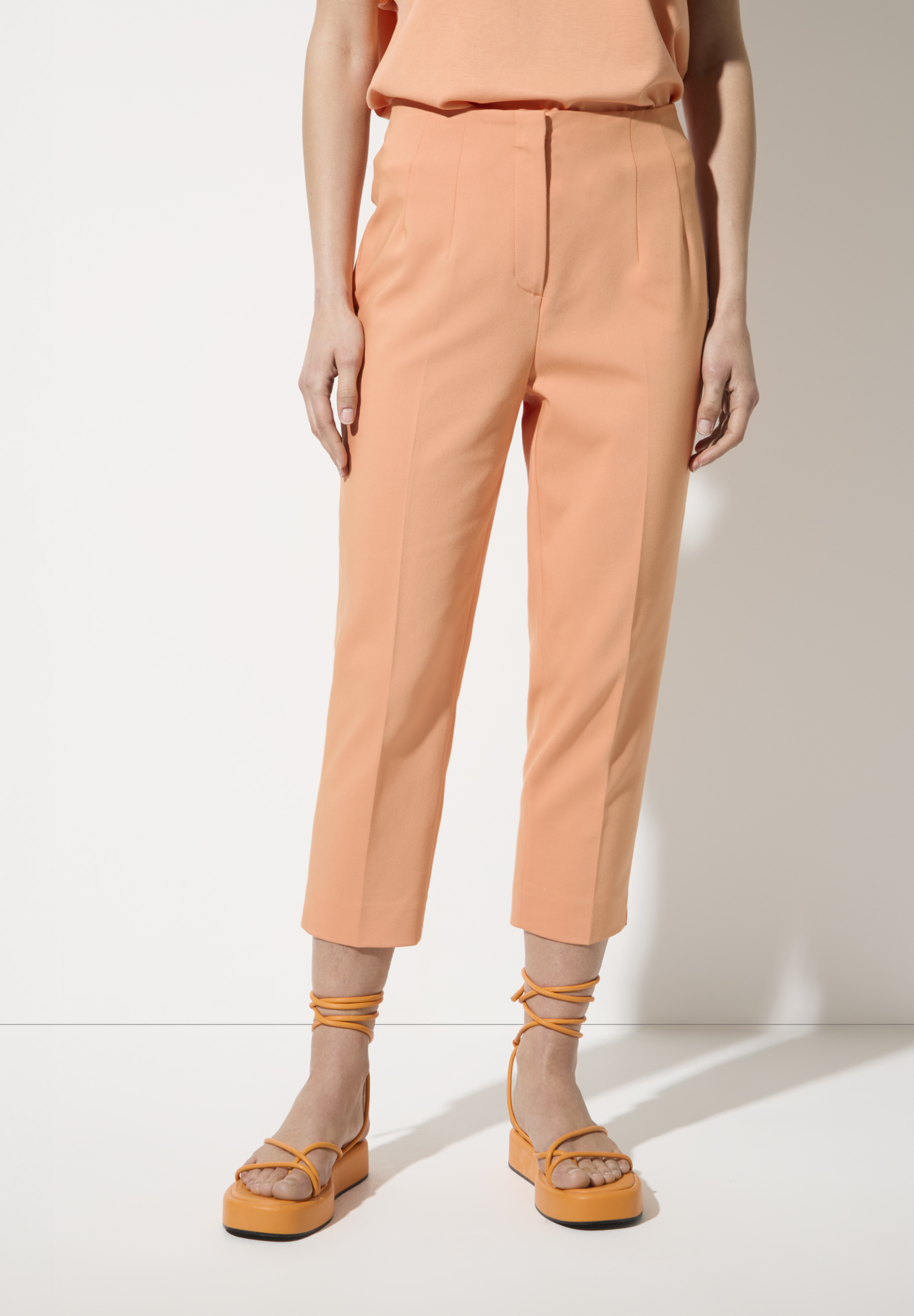 Eine Frau trägt eine MORE & MORE Hose aus Baumwollmischung und orangefarbene Sandalen mit Plateau-Absatz.