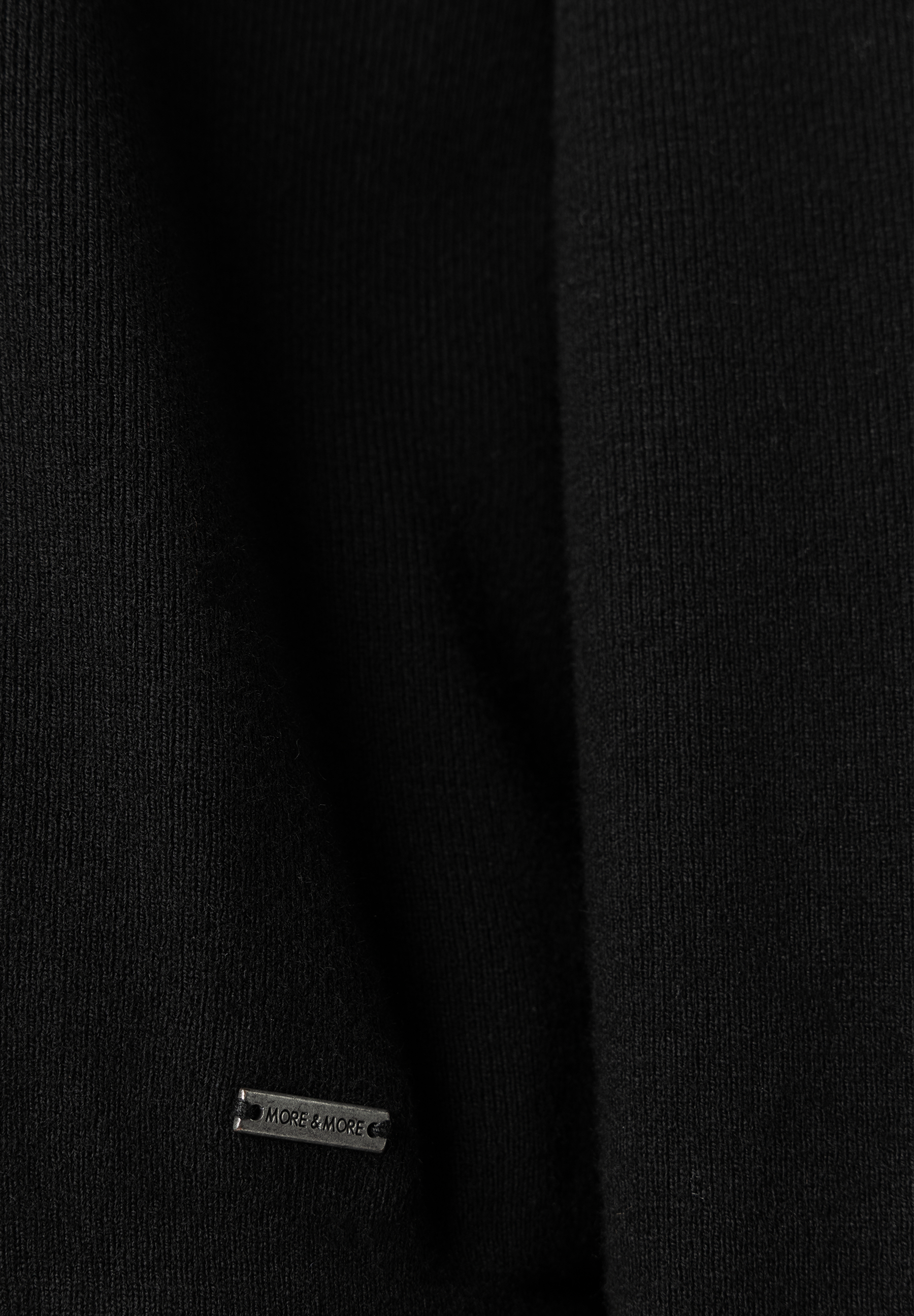 Nahaufnahme eines schwarzen MORE & MORE Pullovers mit feinem Rippstrickmuster und einem dezenten Metall-Logo.