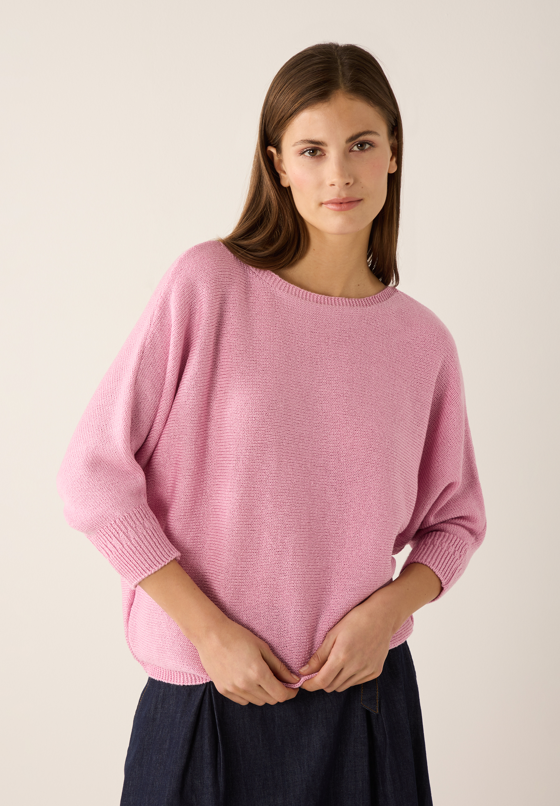 Eine Frau mit MORE & MORE Strickware in Rosa vor hellem Hintergrund. Eine Frau mit MORE & MORE Strickware in Rosa vor hellem Hintergrund.
