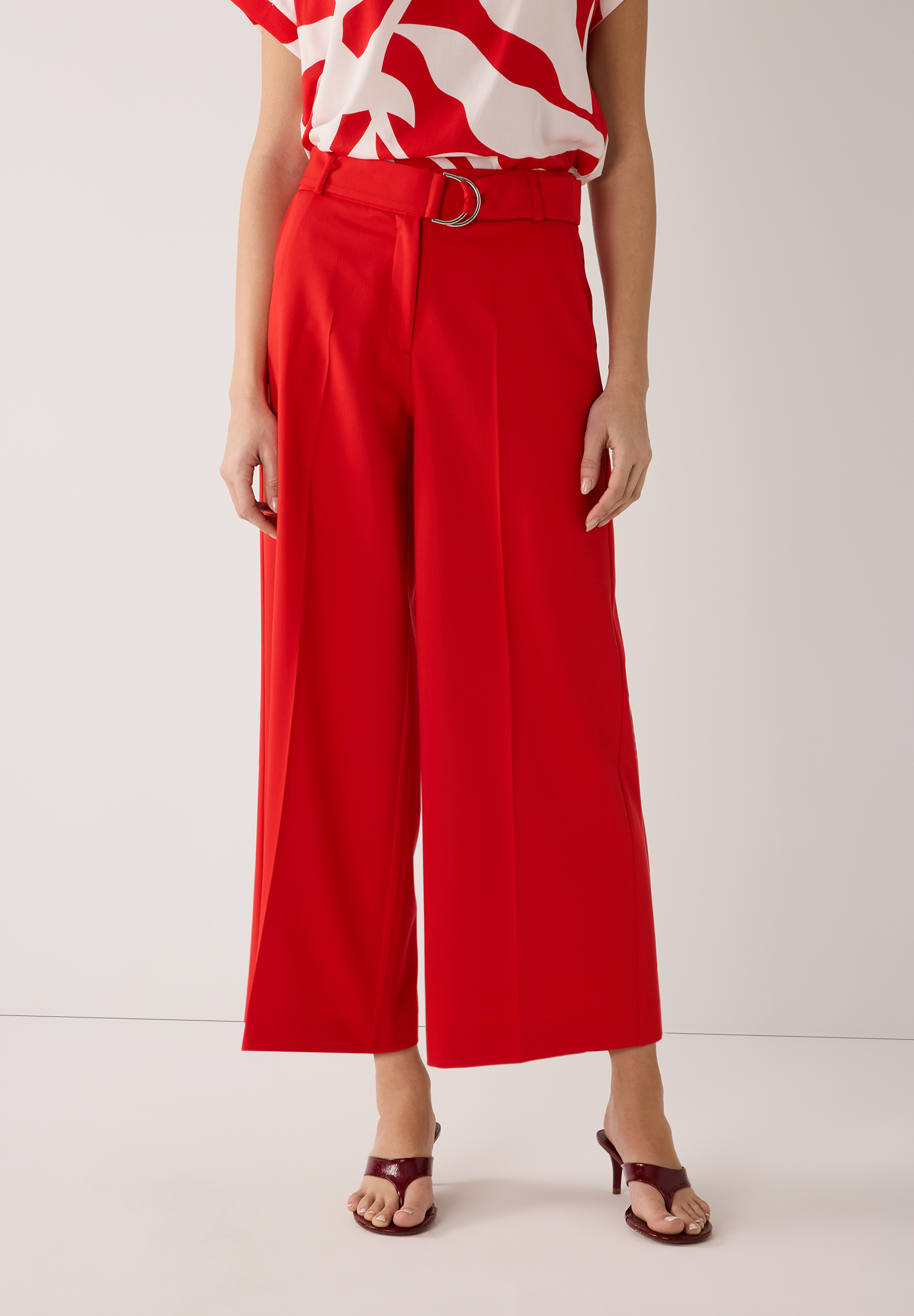 Eine rote, fließende MORE & MORE Webhose mit Gürtel und dazu passenden roten Schuhen.