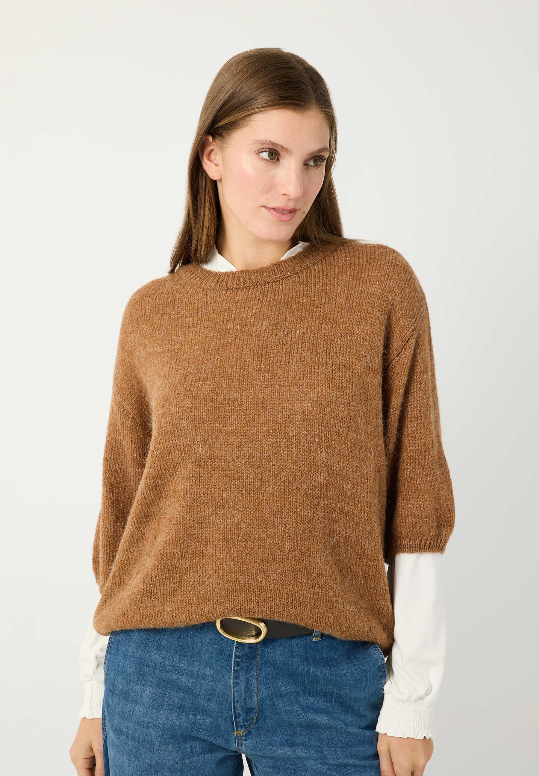 MORE & MORE Pullover: Eine Frau trägt einen wärmenden, braunen Strickpullover über einem weißen Oberteil und Jeans.