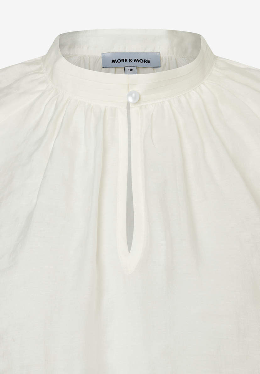 Nahaufnahme einer weißen MORE & MORE Bluse mit Stehkragen und Knopf. Nahaufnahme einer weißen MORE & MORE Bluse mit Stehkragen und Knopf.