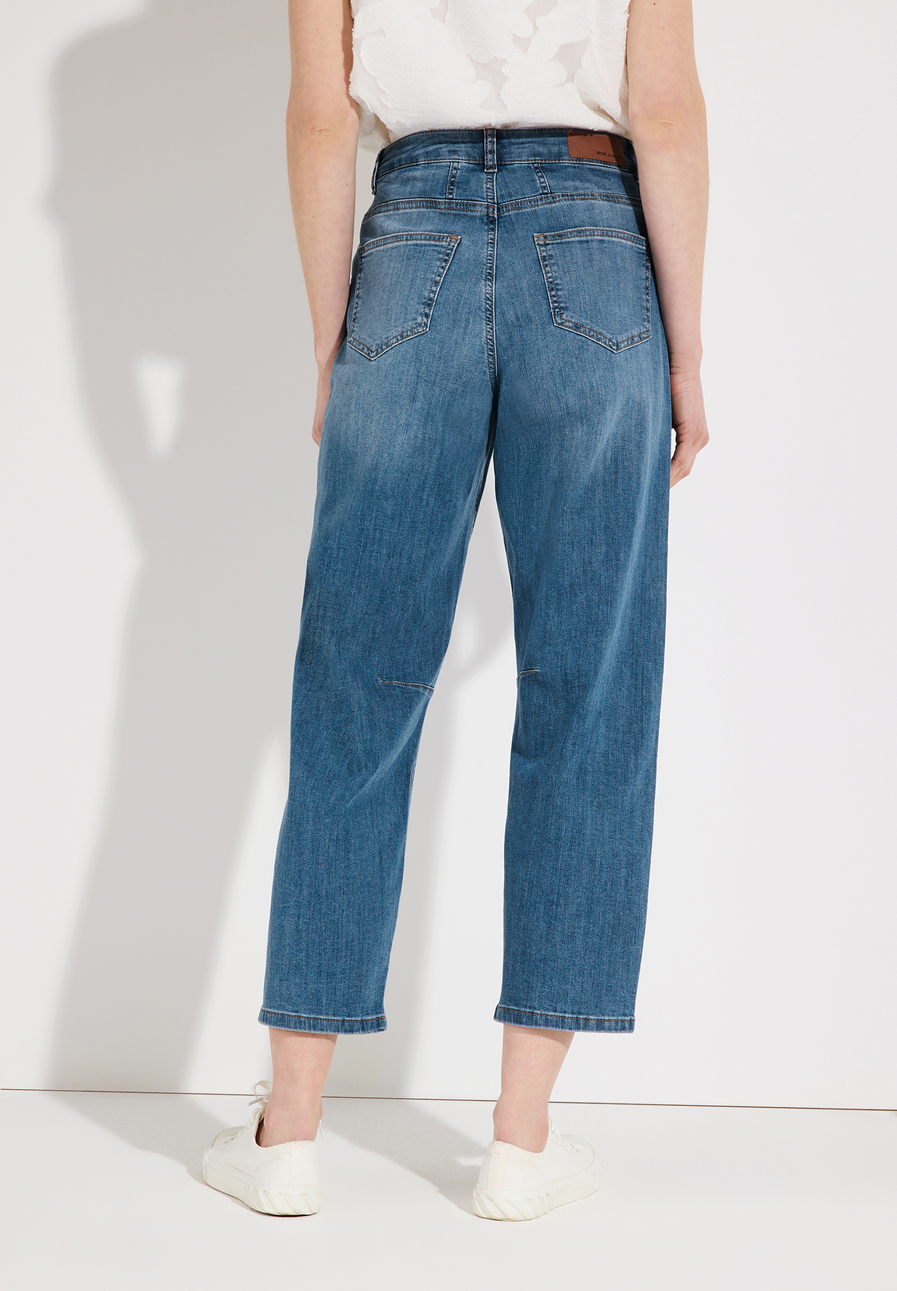 Nahaufnahme der Rückansicht einer Frau mit MORE & MORE Denim Jeans und weißen Schuhen. Nahaufnahme der Rückansicht einer Frau mit MORE & MORE Denim Jeans und weißen Schuhen.