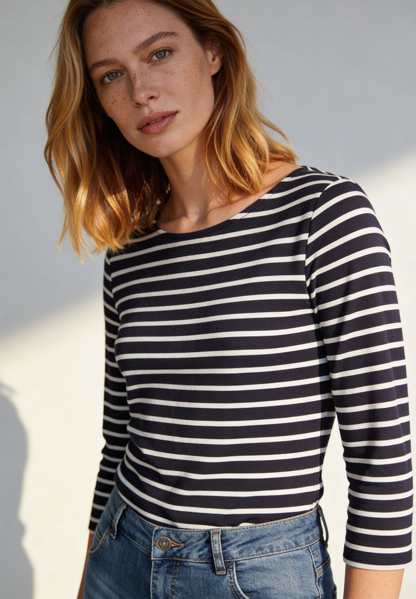 Eine Frau mit Sommersprossen trägt ein gestreiftes MORE & MORE Jersey-Top mit langen Ärmeln und Jeans. Eine Frau mit Sommersprossen trägt ein gestreiftes MORE & MORE Jersey-Top mit langen Ärmeln und Jeans.