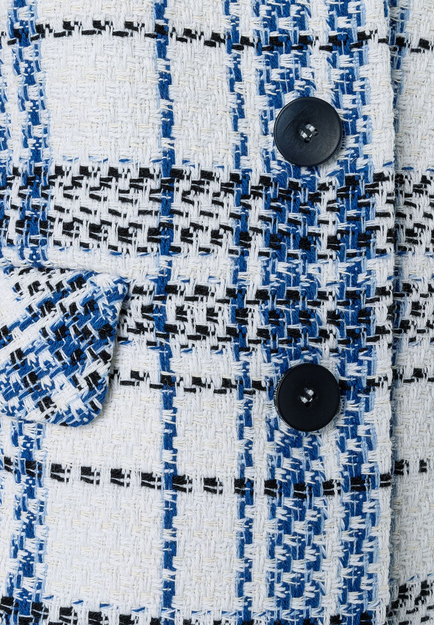 Detailansicht eines MORE & MORE Bouclé-Blazers mit blau-schwarz-weißem Karomuster und dunklen Knöpfen. Detailansicht eines MORE & MORE Bouclé-Blazers mit blau-schwarz-weißem Karomuster und dunklen Knöpfen.