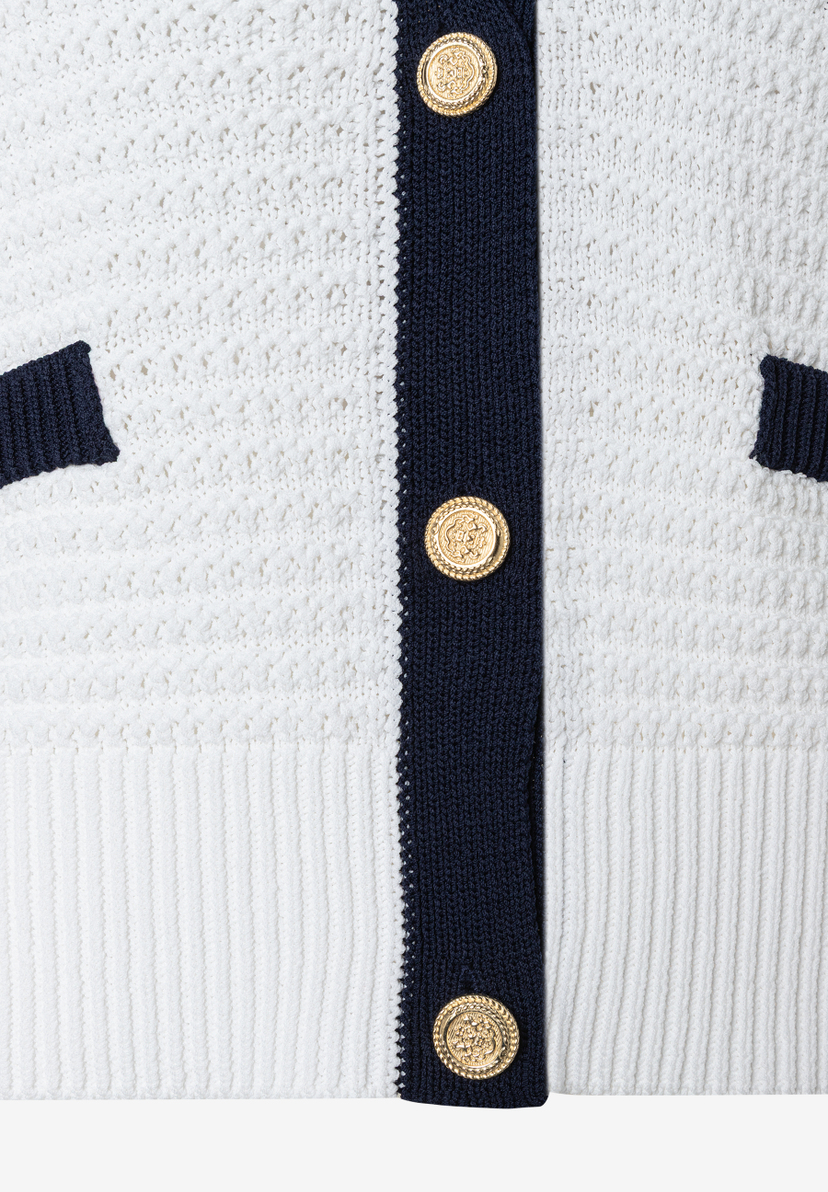 Nahaufnahme eines weißen MORE & MORE Strickoberteils mit blauen Akzenten und goldenen Knöpfen. Nahaufnahme eines weißen MORE & MORE Strickoberteils mit blauen Akzenten und goldenen Knöpfen.