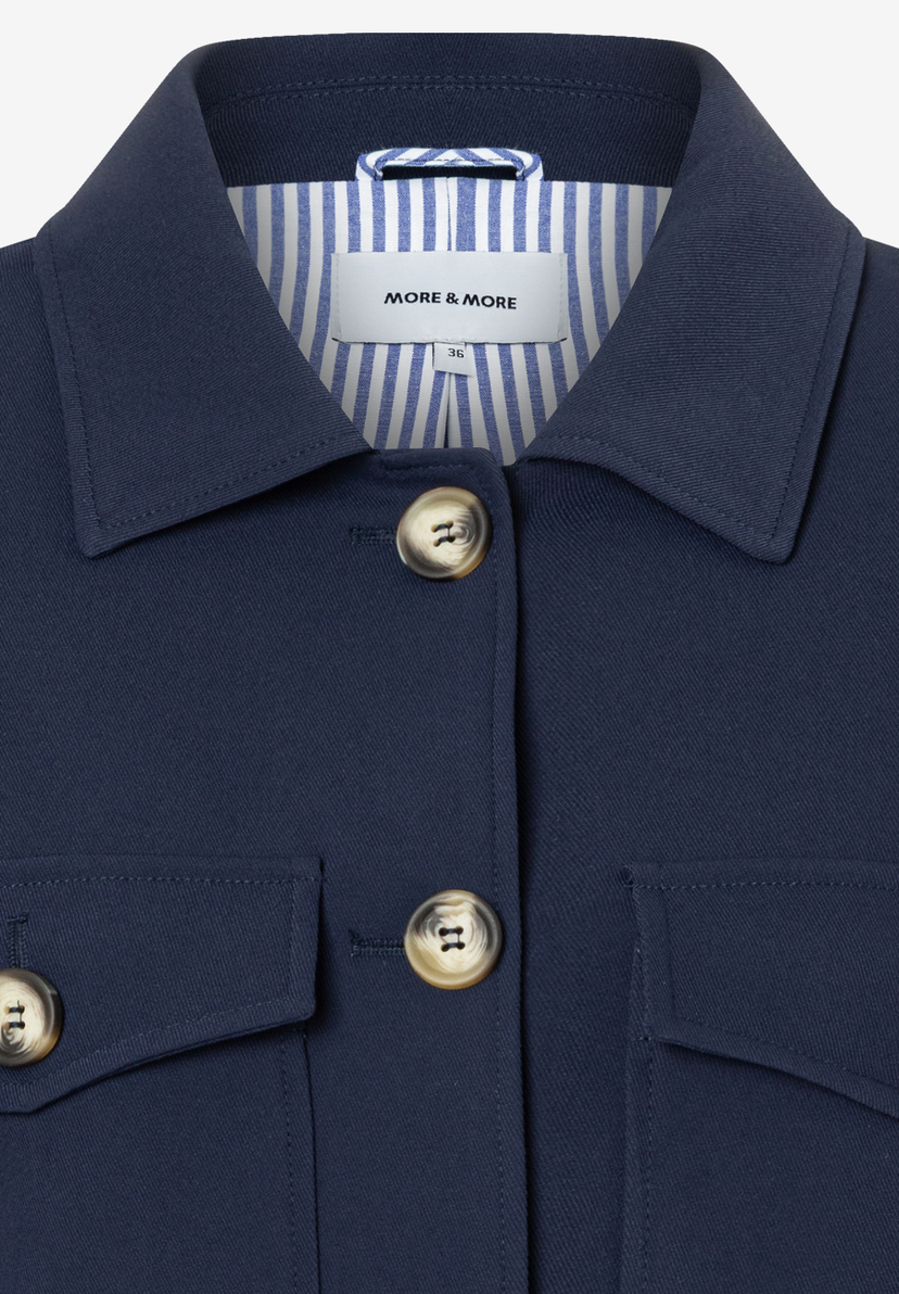 Nahaufnahme eines blauen MORE & MORE Blazers mit Knöpfen und Kragen. Nahaufnahme eines blauen MORE & MORE Blazers mit Knöpfen und Kragen.