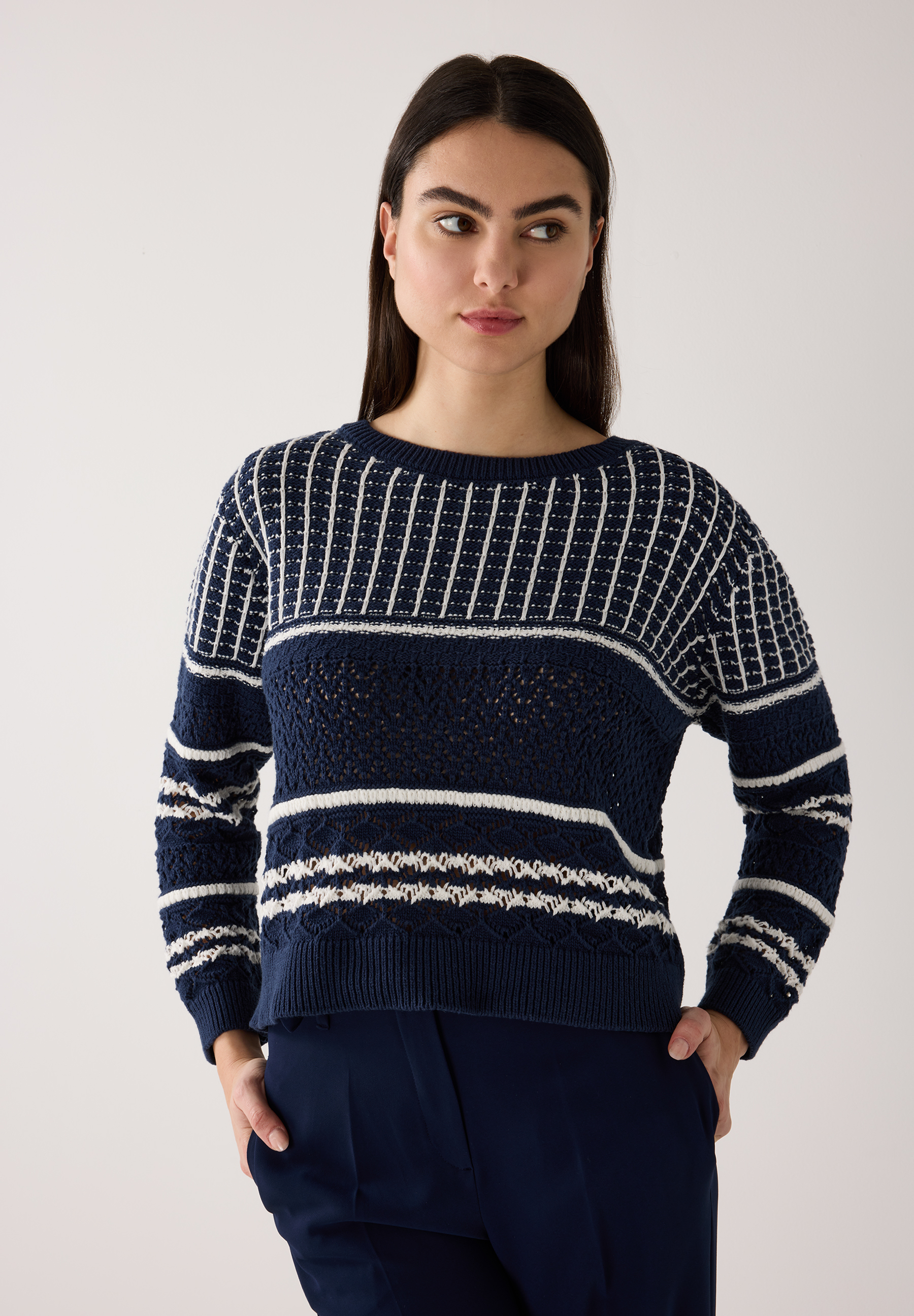 Eine Frau trägt einen dunkelblauen Strick-Pullover von MORE & MORE mit weißen Streifen.