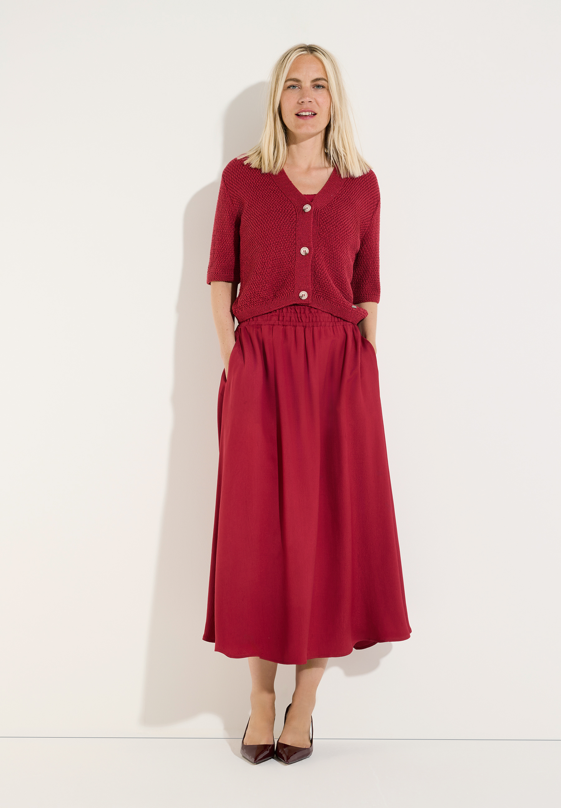 MORE & MORE Midirock in Rot mit einem passenden, kurzärmeligen Strickpullover. Die blonde Frau trägt dazu elegante, dunkelrote Pumps. MORE & MORE Midirock in Rot mit einem passenden, kurzärmeligen Strickpullover. Die blonde Frau trägt dazu elegante, dunkelrote Pumps.