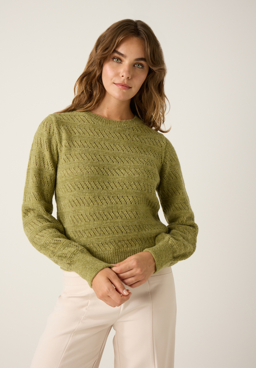 Eine Frau mit braunen, gewellten Haaren trägt einen grünen Strukturstrick-Pullover von MORE & MORE und eine helle Hose vor einem hellen Hintergrund. Eine Frau mit braunen, gewellten Haaren trägt einen grünen Strukturstrick-Pullover von MORE & MORE und eine helle Hose vor einem hellen Hintergrund.