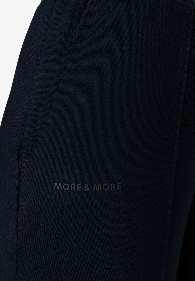 Dunkelblaue MORE & MORE Jeans mit subtilem Logo auf dem Oberschenkel und sichtbaren Nähten. Dunkelblaue MORE & MORE Jeans mit subtilem Logo auf dem Oberschenkel und sichtbaren Nähten.