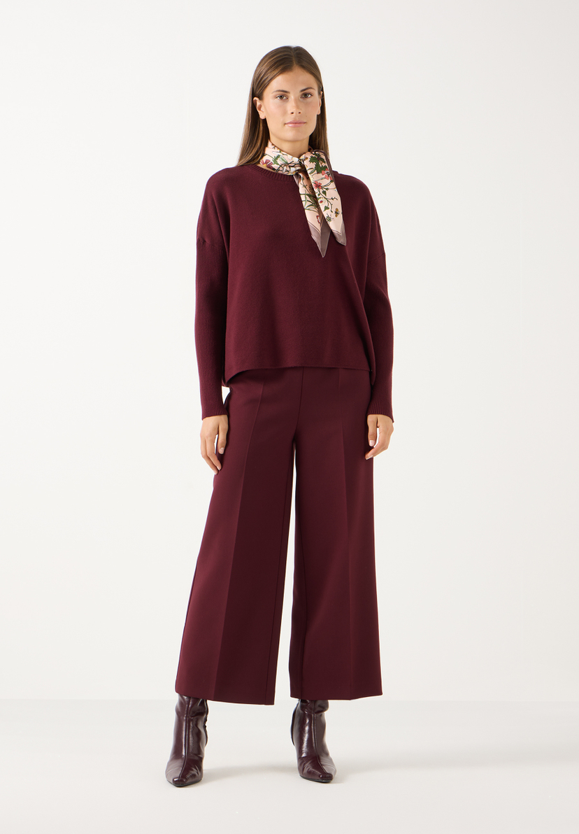 MORE & MORE Hose: Eine Frau trägt eine weinrote MORE & MORE Culotte Hose und einen passenden weinroten Pullover mit einem gemusterten Schal und eleganten Stiefeln.