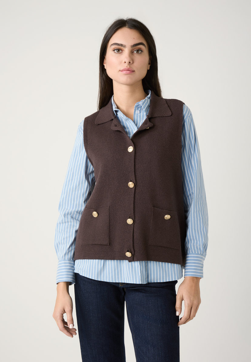 Eine Frau in einem MORE & MORE Strickoberteil mit goldenen Knöpfen, darunter eine blau-weiß gestreifte Bluse und Jeans. Eine Frau in einem MORE & MORE Strickoberteil mit goldenen Knöpfen, darunter eine blau-weiß gestreifte Bluse und Jeans.