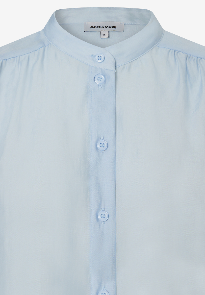 Nahaufnahme einer hellblauen MORE & MORE Bluse mit Knopfleiste und Stehkragen. Nahaufnahme einer hellblauen MORE & MORE Bluse mit Knopfleiste und Stehkragen.