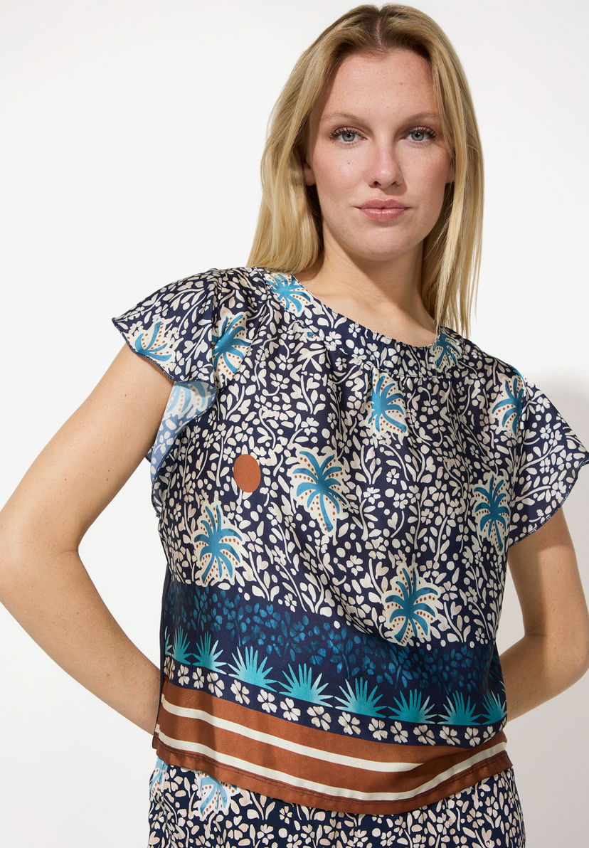 Eine Frau mit einem MORE & MORE Top mit blau-weißem Blumenmuster posiert vor einem weißen Hintergrund. Eine Frau mit einem MORE & MORE Top mit blau-weißem Blumenmuster posiert vor einem weißen Hintergrund.