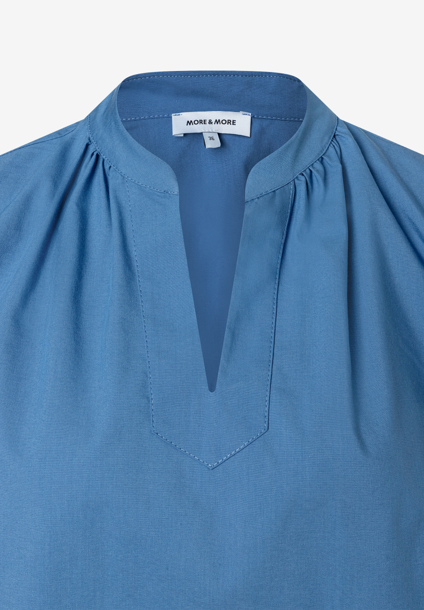 Nahaufnahme einer blauen MORE & MORE Bluse mit V-Ausschnitt. Nahaufnahme einer blauen MORE & MORE Bluse mit V-Ausschnitt.