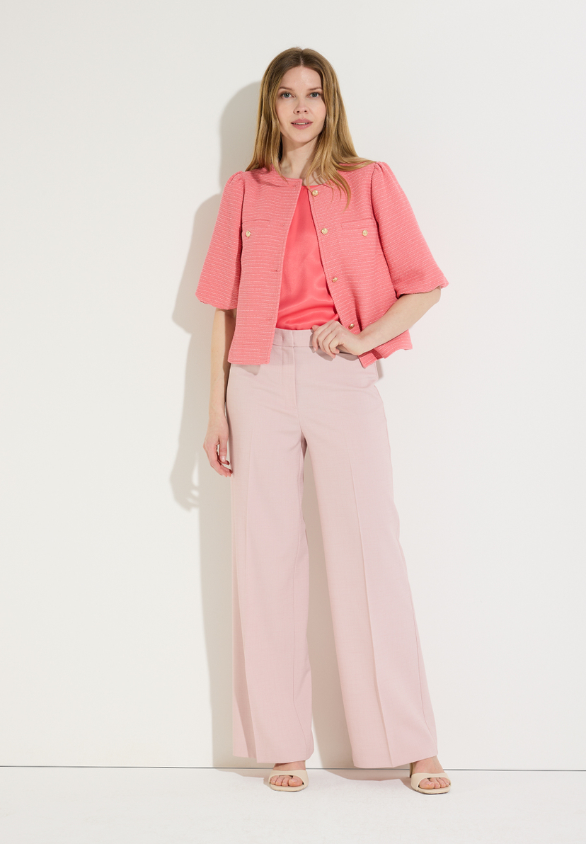 Eine Frau, die einen korallenroten Bouclé-Blazer von MORE & MORE zu braunen Hosen und braunen Ledersandalen trägt. Eine Frau, die einen korallenroten Bouclé-Blazer von MORE & MORE zu braunen Hosen und braunen Ledersandalen trägt.