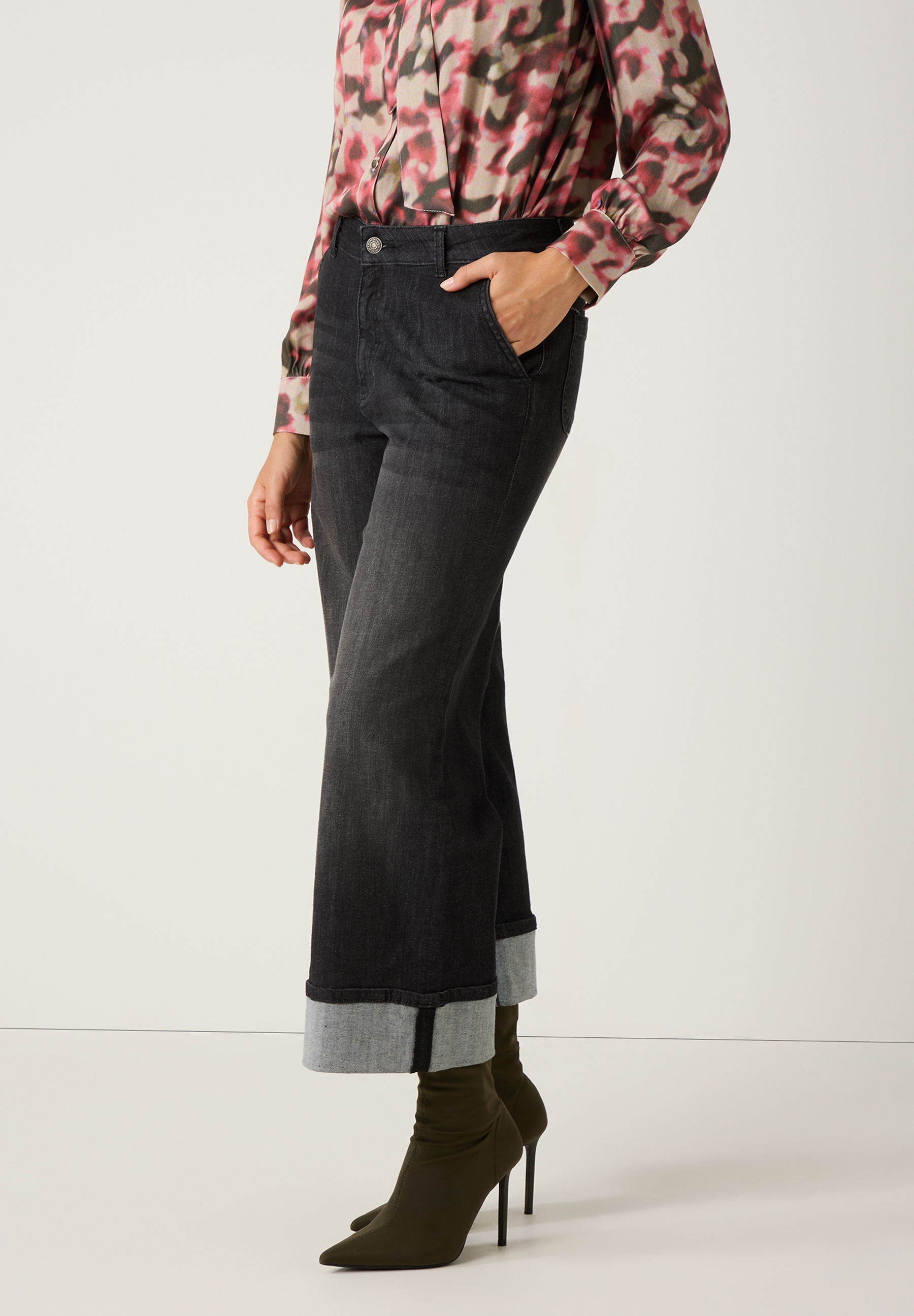 Eine Frau in MORE & MORE Jeanshose aus Denim, kombiniert mit einer farbenfrohen Bluse und Stiefeln. Eine Frau in MORE & MORE Jeanshose aus Denim, kombiniert mit einer farbenfrohen Bluse und Stiefeln.