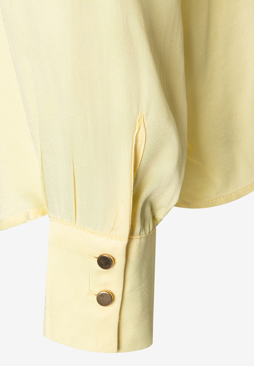Nahaufnahme eines Manschettendetails der MORE & MORE Bluse aus gelbem Satin mit glänzenden goldenen Knöpfen. Nahaufnahme eines Manschettendetails der MORE & MORE Bluse aus gelbem Satin mit glänzenden goldenen Knöpfen.