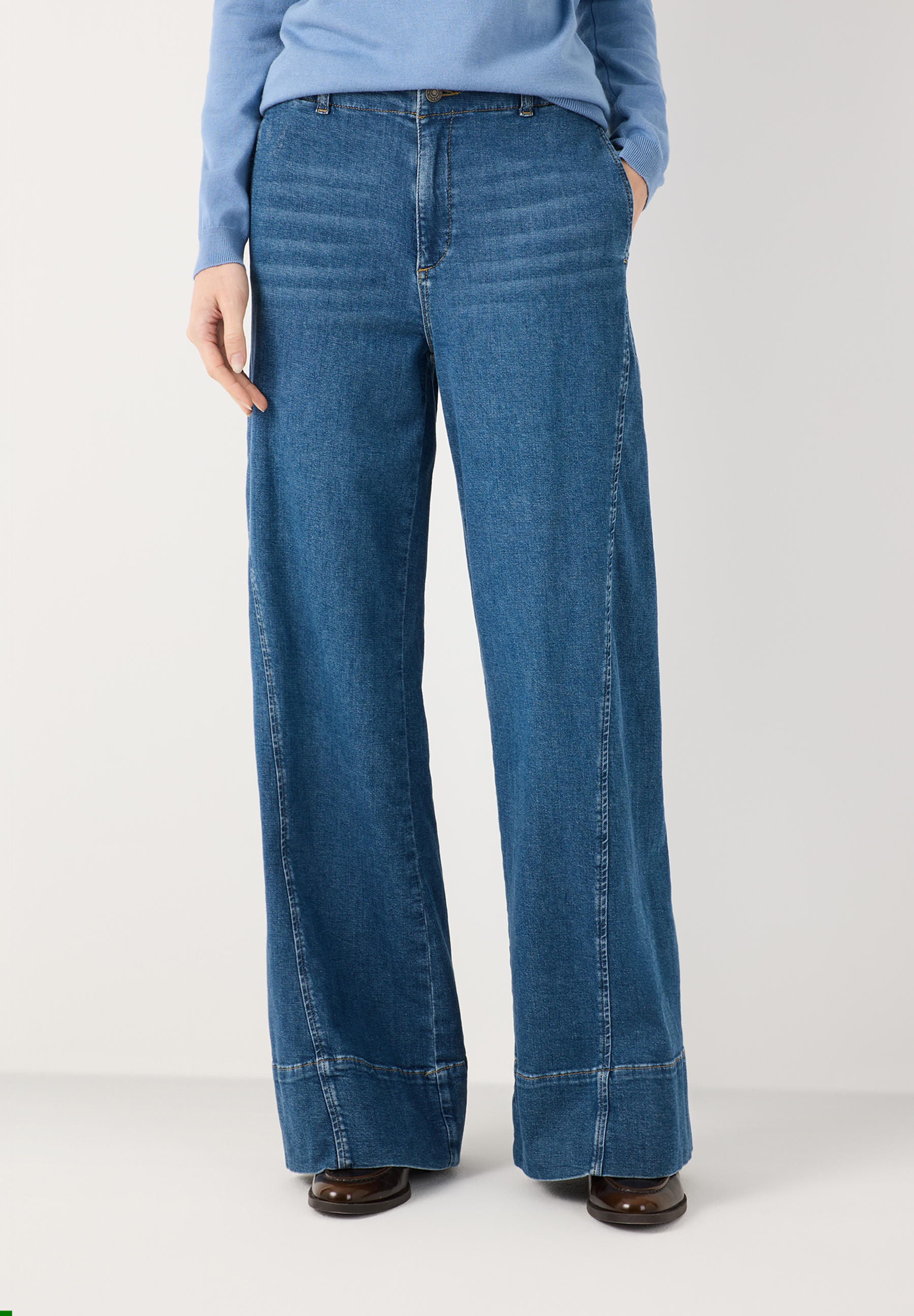 MORE & MORE Damen-Jeans in Dunkelblau, ausgestellter Schnitt. Eine Hand steckt lässig in der Hosentasche.