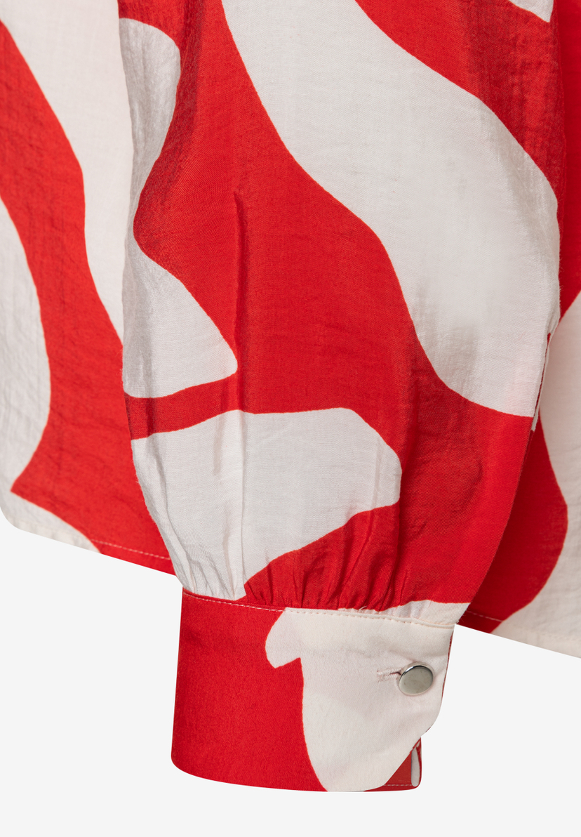 Nahaufnahme einer rot-weiß gemusterten MORE & MORE Bluse mit Knopf am Ärmel. Nahaufnahme einer rot-weiß gemusterten MORE & MORE Bluse mit Knopf am Ärmel.