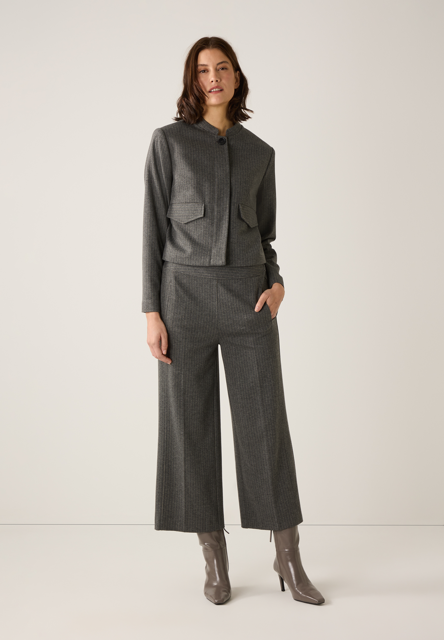 Eine Frau trägt ein graues MORE & MORE Oberteil aus Jersey und eine passende Hose mit Stiefeln vor einem hellen Hintergrund. Eine Frau trägt ein graues MORE & MORE Oberteil aus Jersey und eine passende Hose mit Stiefeln vor einem hellen Hintergrund.