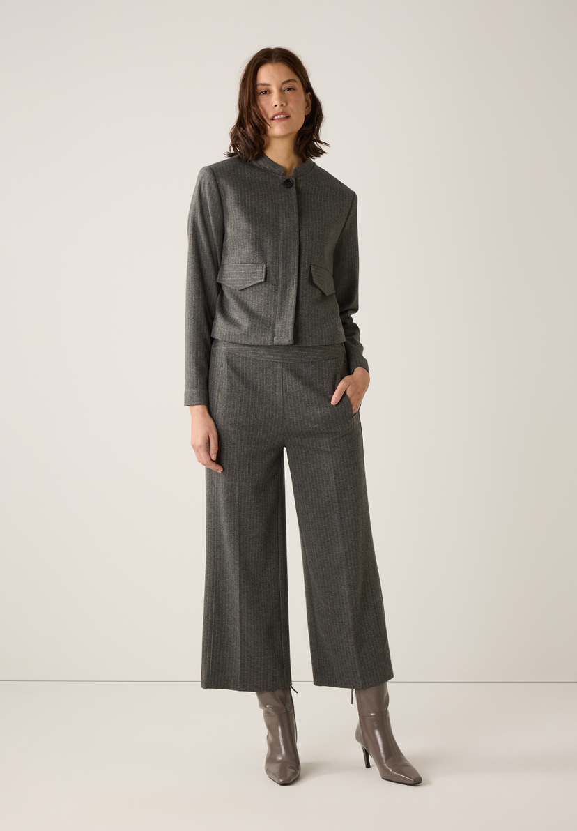 Eine Frau trägt ein graues MORE & MORE Oberteil aus Jersey und eine passende Hose mit Stiefeln vor einem hellen Hintergrund. Eine Frau trägt ein graues MORE & MORE Oberteil aus Jersey und eine passende Hose mit Stiefeln vor einem hellen Hintergrund.