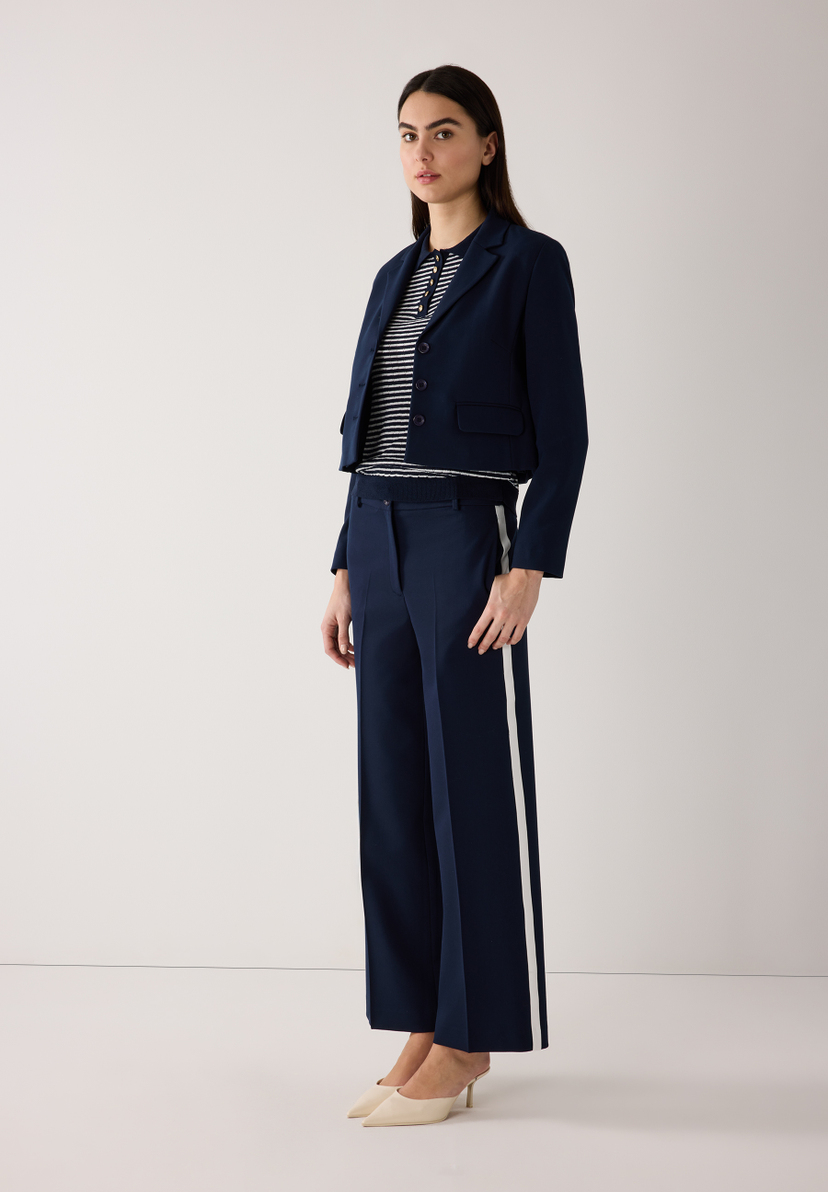 Eine Frau in einem marineblauen MORE & MORE Blazer und passender Hose mit weißem Seitenstreifen. Eine Frau in einem marineblauen MORE & MORE Blazer und passender Hose mit weißem Seitenstreifen.