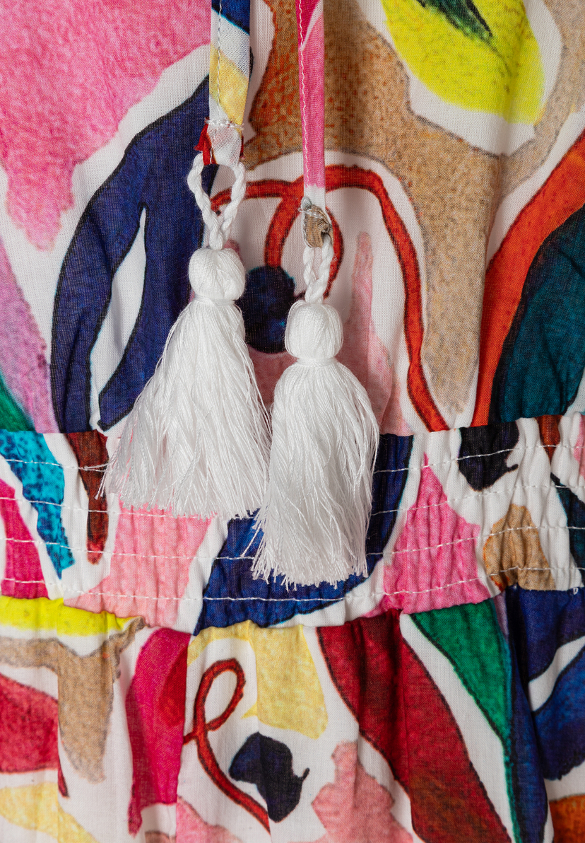 Detailansicht eines MORE & MORE Oberteils aus leichtem Voile-Material mit bunten Mustern und weißen Quasten. Detailansicht eines MORE & MORE Oberteils aus leichtem Voile-Material mit bunten Mustern und weißen Quasten.