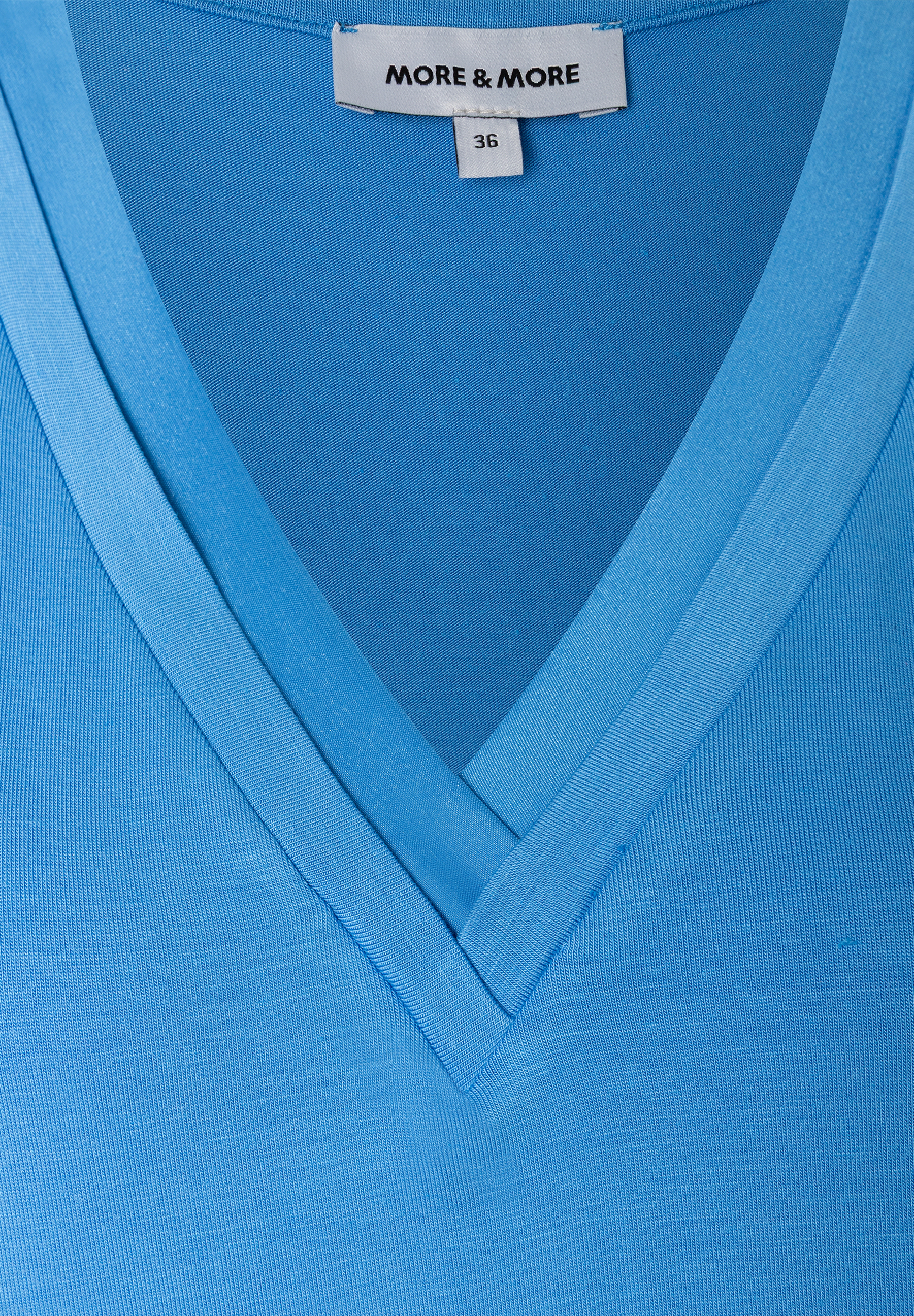 Nahaufnahme eines hellblauen MORE & MORE T-Shirts mit V-Ausschnitt und Etikett mit Größenangabe.