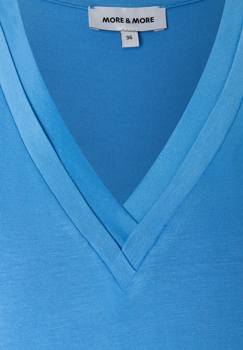 Nahaufnahme eines hellblauen MORE & MORE T-Shirts mit V-Ausschnitt und Etikett mit Größenangabe.