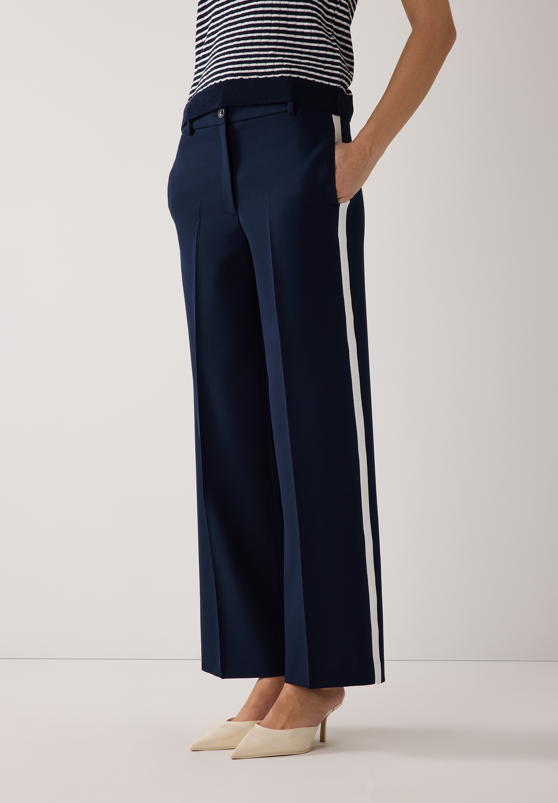 Eine MORE & MORE Hose in Dunkelblau mit weißem Seitenstreifen, kombiniert mit einem gestreiften Oberteil und hellen Schuhen.