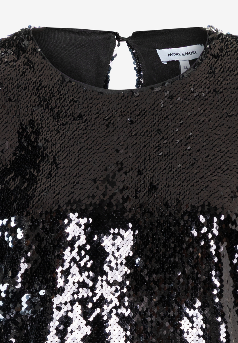 Nahaufnahme einer schwarzen Paillettenbluse von MORE & MORE mit glänzender Optik. Nahaufnahme einer schwarzen Paillettenbluse von MORE & MORE mit glänzender Optik.