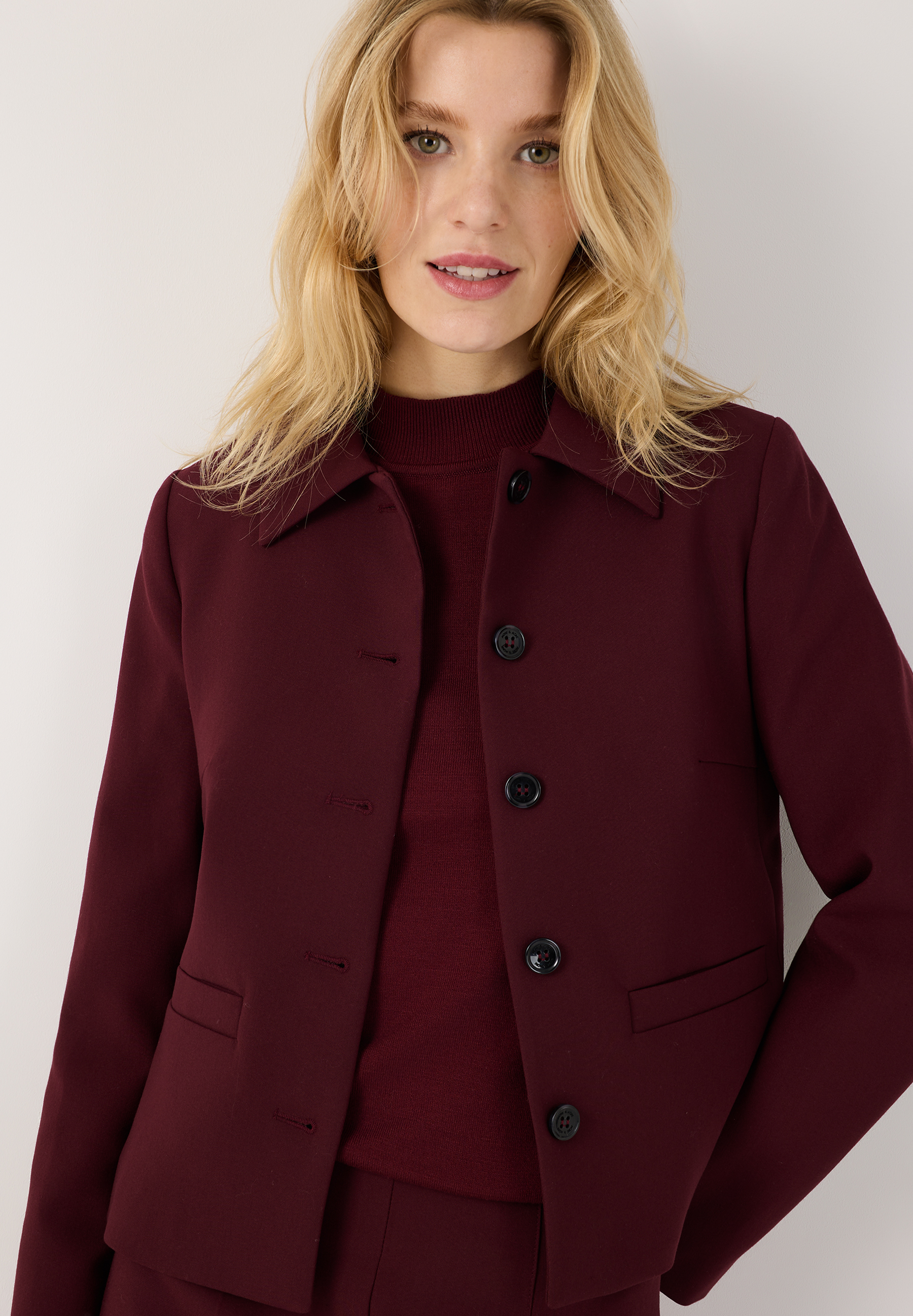 MORE & MORE Kurzblazer aus bordeauxroter Webware. Eine junge Frau trägt den taillierten Blazer mit langen Ärmeln.