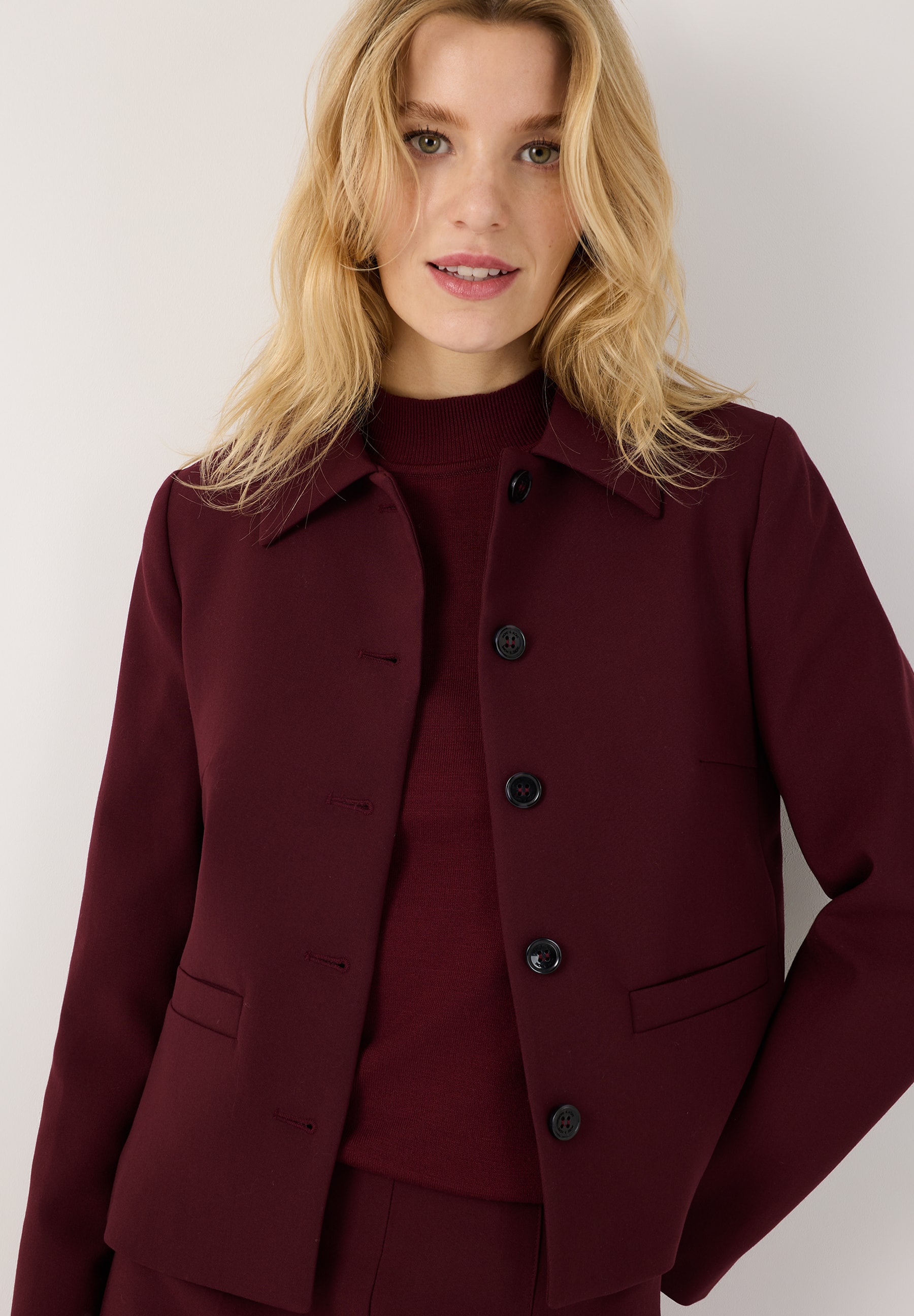 MORE & MORE Kurzblazer aus bordeauxroter Webware. Eine junge Frau trägt den taillierten Blazer mit langen Ärmeln.