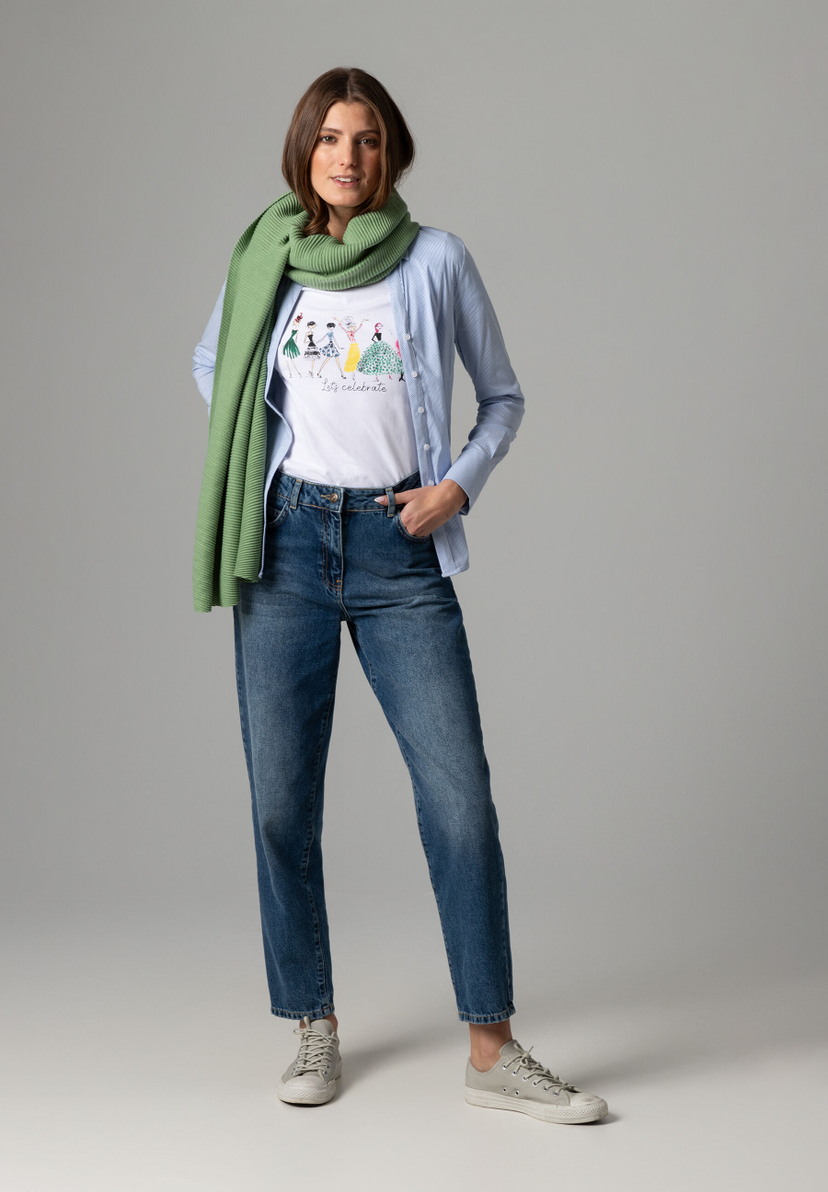 Eine Frau mit einem MORE & MORE Oberteil, Jeans und einem grünen Schal vor einem grauen Hintergrund. Eine Frau mit einem MORE & MORE Oberteil, Jeans und einem grünen Schal vor einem grauen Hintergrund.