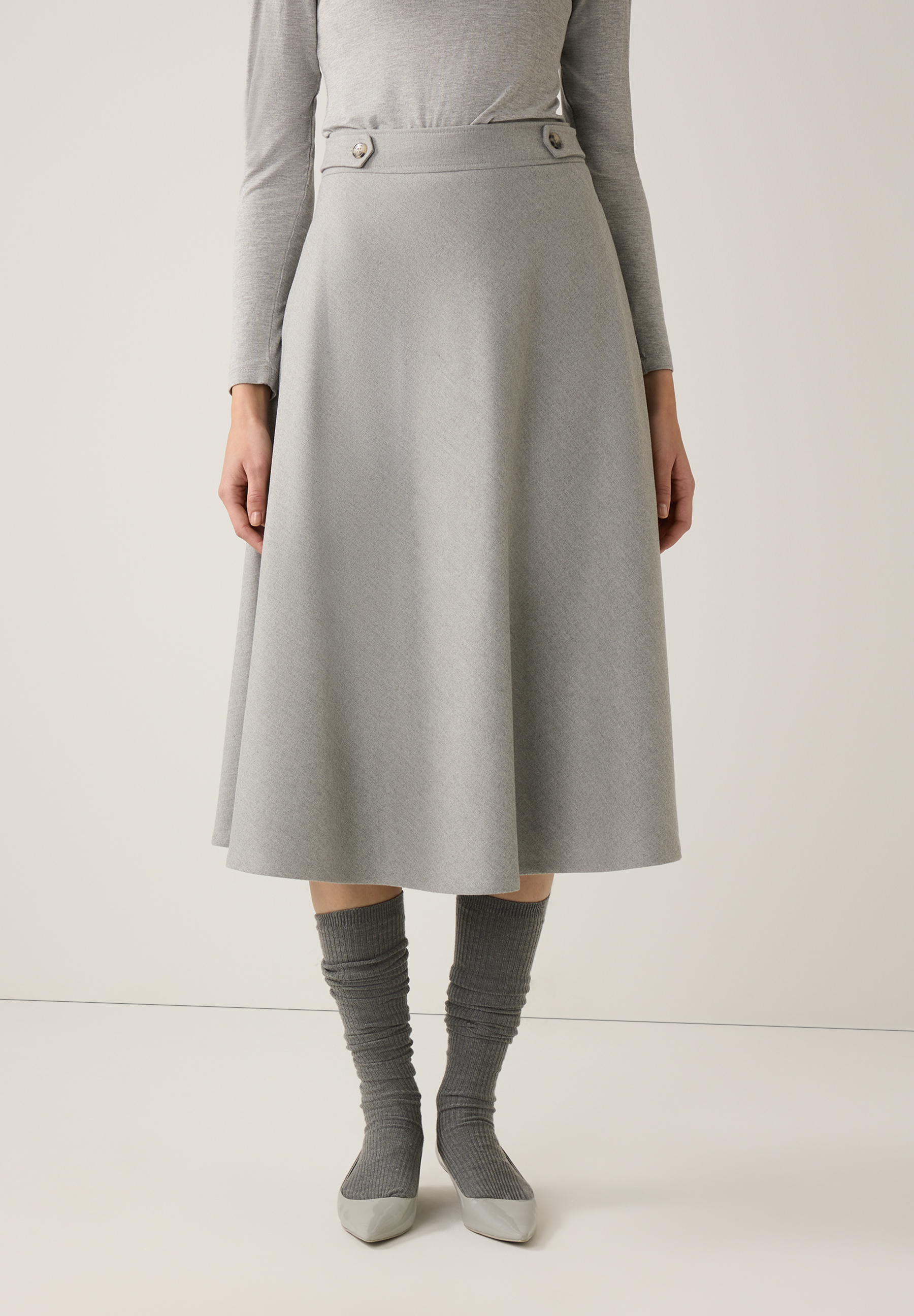 Ein grauer MORE & MORE Rock in A-Linie mit Knöpfen am Bund, kombiniert mit passenden Strümpfen und Schuhen.