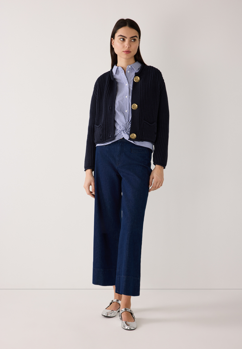 Eine Frau trägt einen marineblauen Rippstrick-Cardigan von MORE & MORE mit goldenen Knöpfen, ein gestreiftes Hemd und eine Jeanshose. Eine Frau trägt einen marineblauen Rippstrick-Cardigan von MORE & MORE mit goldenen Knöpfen, ein gestreiftes Hemd und eine Jeanshose.