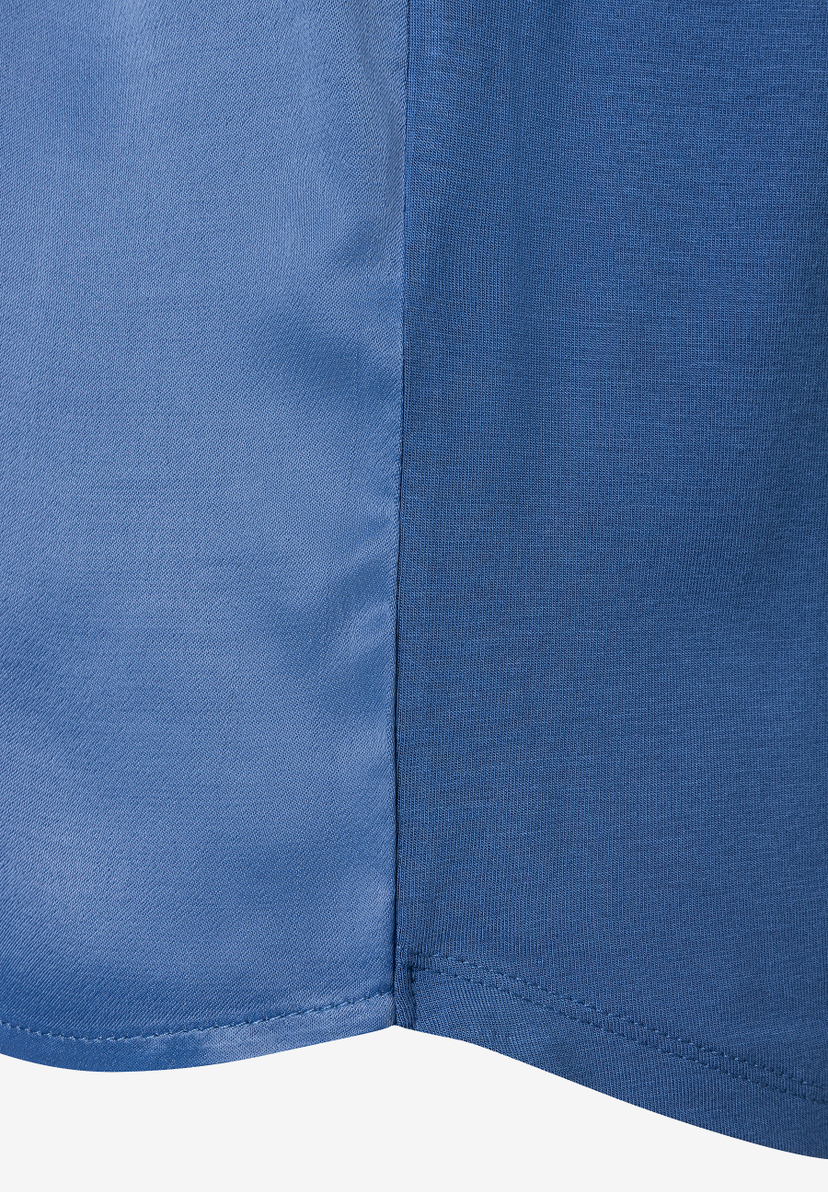 Nahaufnahme eines blauen MORE & MORE Oberteils mit Naht und unterschiedlichen Stoffstrukturen. Nahaufnahme eines blauen MORE & MORE Oberteils mit Naht und unterschiedlichen Stoffstrukturen.