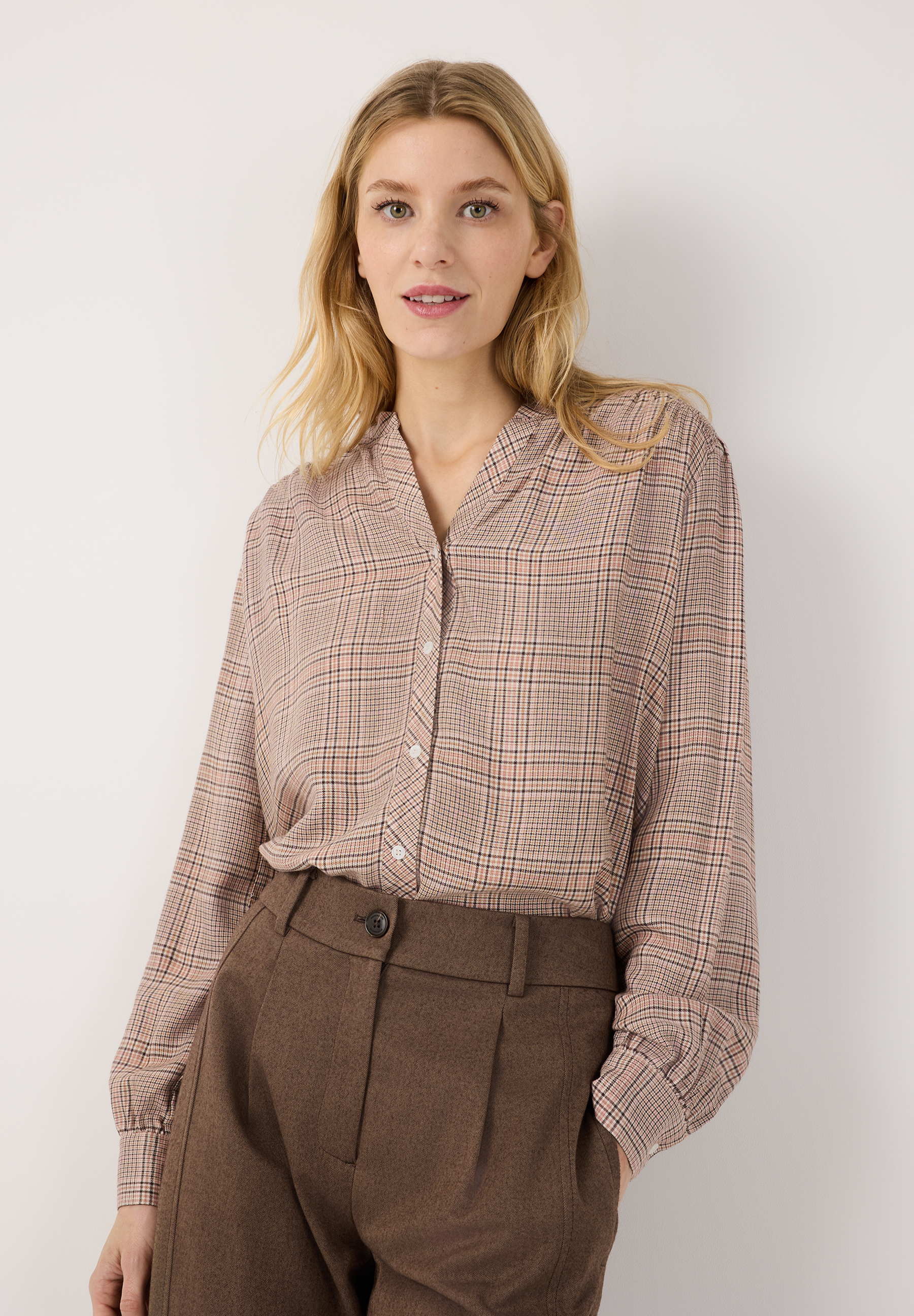 MORE & MORE Bluse: Eine junge Frau trägt eine karierte Bluse und braune Hose, die Hände in den Hosentaschen.